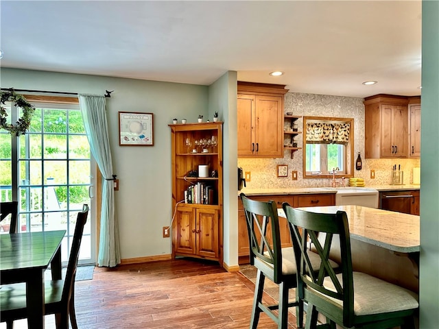 kitchen featuring backsplash, stainless steel dishwasher, light stone countertops, and light hardwood / wood-style flooring