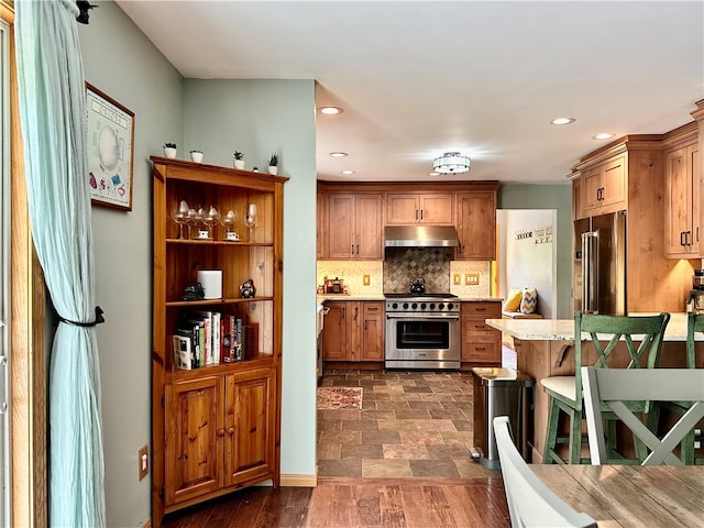 kitchen with a kitchen breakfast bar, backsplash, premium appliances, and dark hardwood / wood-style flooring