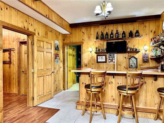 bar featuring hanging light fixtures, wooden walls, beam ceiling, and light tile patterned floors