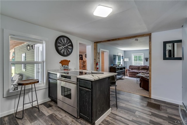 kitchen with stainless steel range with electric stovetop, dark hardwood / wood-style flooring, a breakfast bar area, and kitchen peninsula