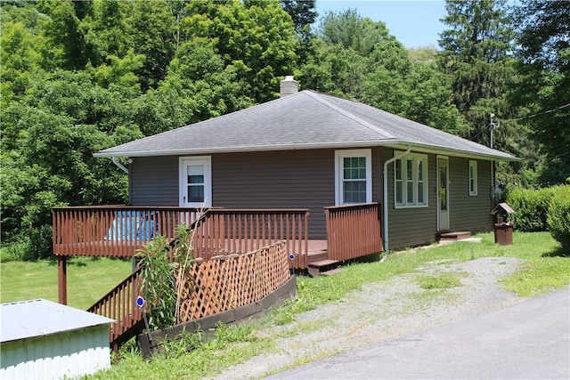 view of front of home featuring a front yard, driveway, a shingled roof, a chimney, and a deck