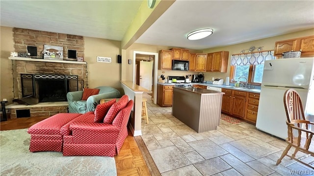 kitchen featuring stove, white refrigerator, a stone fireplace, sink, and a kitchen island