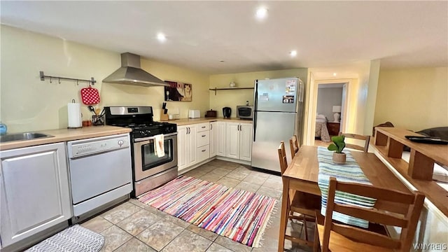 kitchen featuring white cabinetry, light tile patterned floors, wall chimney range hood, and appliances with stainless steel finishes