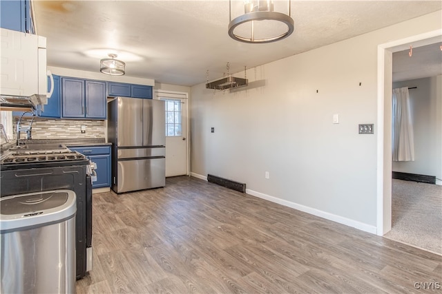 kitchen with blue cabinetry, stainless steel appliances, backsplash, and light hardwood / wood-style floors