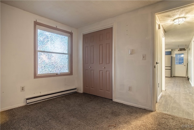 unfurnished bedroom featuring a closet, a textured ceiling, baseboard heating, and carpet flooring