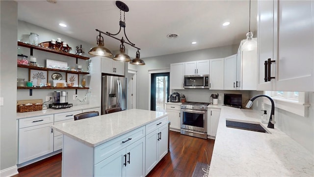 kitchen with light stone counters, stainless steel appliances, sink, pendant lighting, and white cabinetry