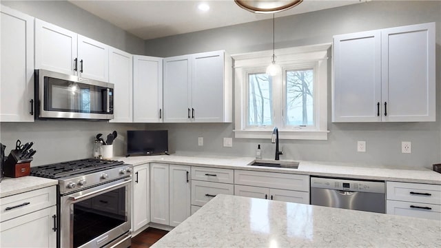 kitchen with white cabinetry, sink, light stone countertops, hanging light fixtures, and stainless steel appliances