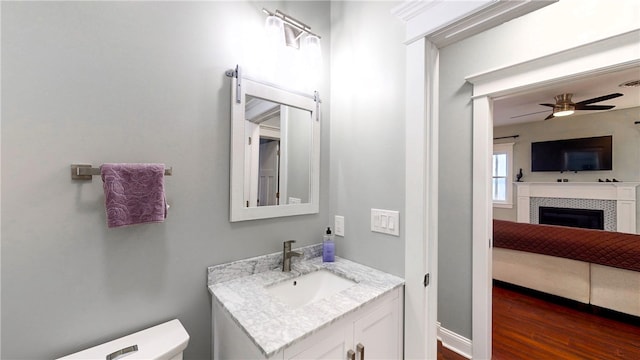 bathroom with a fireplace, vanity, toilet, and ceiling fan