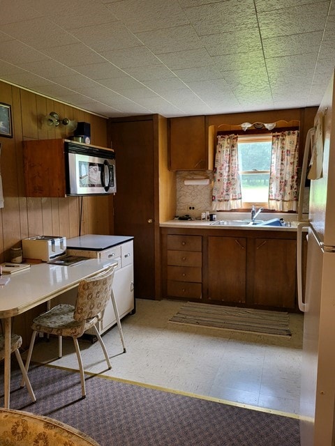 kitchen with light tile patterned flooring, sink, white fridge, and wood walls