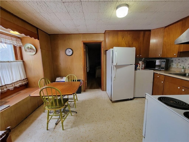 kitchen with sink, white appliances, and wood walls