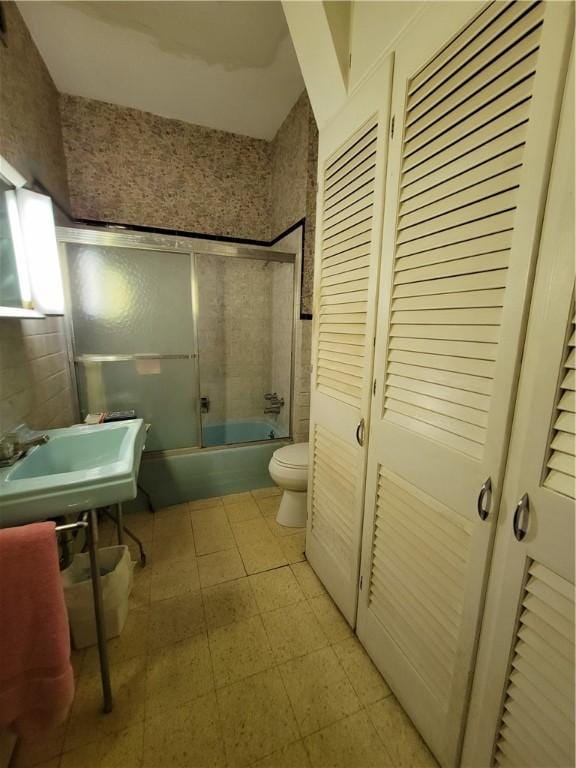 full bathroom featuring sink, combined bath / shower with glass door, and toilet