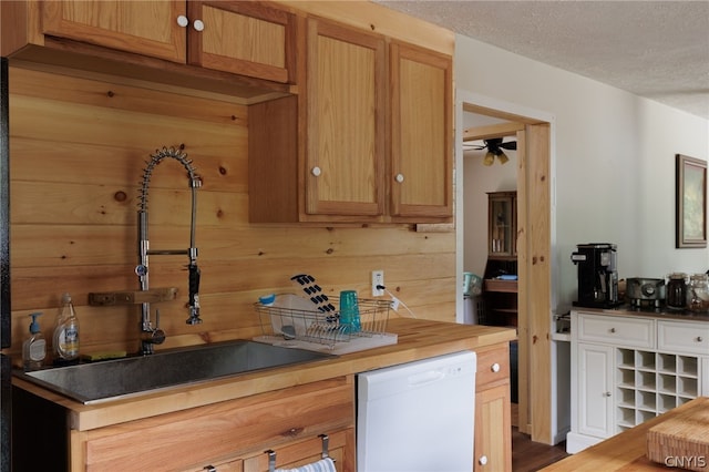 kitchen featuring ceiling fan, white dishwasher, sink, a textured ceiling, and wood walls