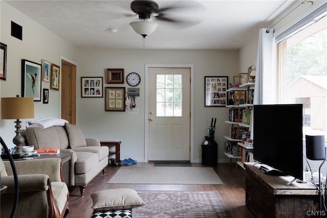 living room with a textured ceiling, ceiling fan, and dark hardwood / wood-style flooring