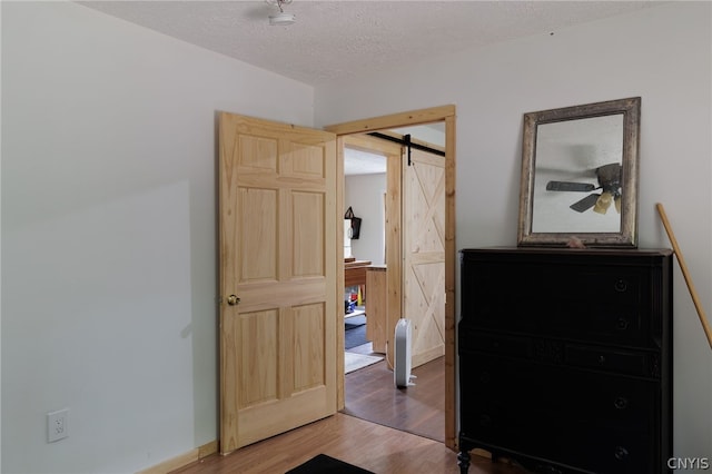 bedroom with a barn door, a textured ceiling, and wood-type flooring