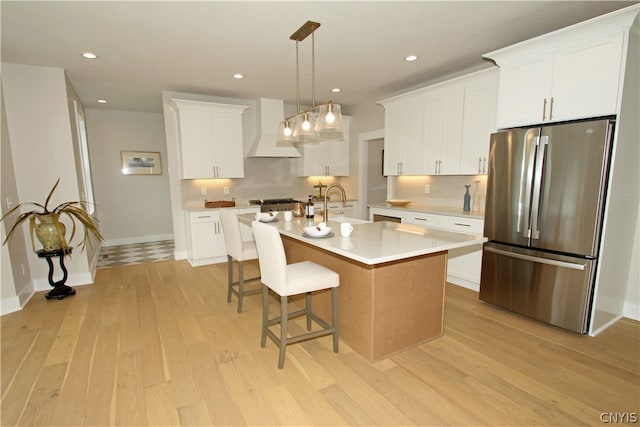 kitchen with light hardwood / wood-style flooring, a center island with sink, appliances with stainless steel finishes, white cabinetry, and premium range hood