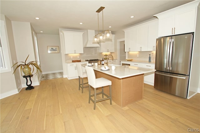 kitchen with an island with sink, hanging light fixtures, white cabinets, light wood-type flooring, and appliances with stainless steel finishes