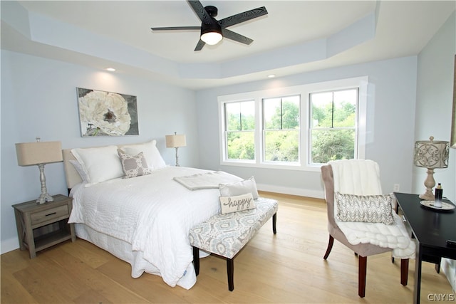 bedroom with a tray ceiling, wood-type flooring, and ceiling fan