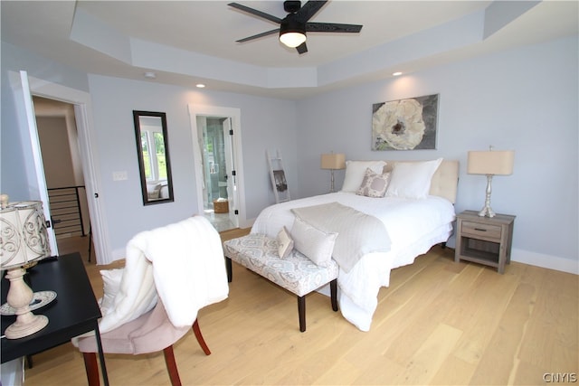 bedroom with light hardwood / wood-style floors, ceiling fan, and a raised ceiling