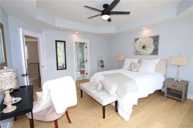 bedroom with light hardwood / wood-style flooring, ceiling fan, and a raised ceiling