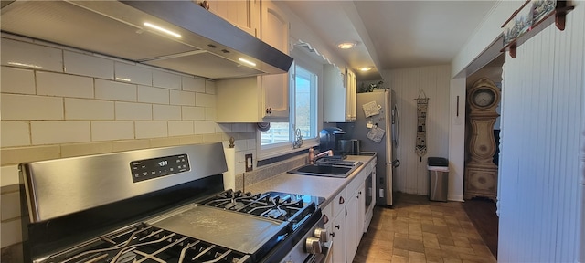 kitchen featuring white cabinetry, wall chimney range hood, stainless steel range with gas cooktop, sink, and backsplash