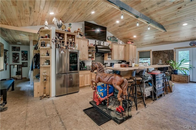 kitchen with vaulted ceiling, light brown cabinets, stainless steel refrigerator, track lighting, and a large island with sink