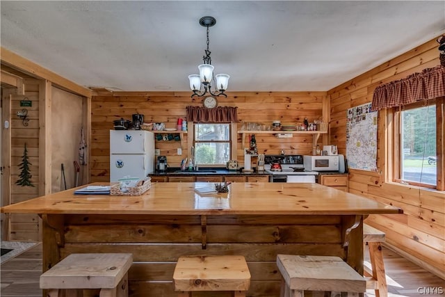 kitchen with pendant lighting, sink, white appliances, a chandelier, and wood walls