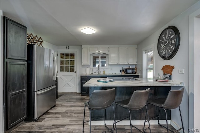 kitchen with hardwood / wood-style flooring, a breakfast bar, white cabinets, and stainless steel refrigerator