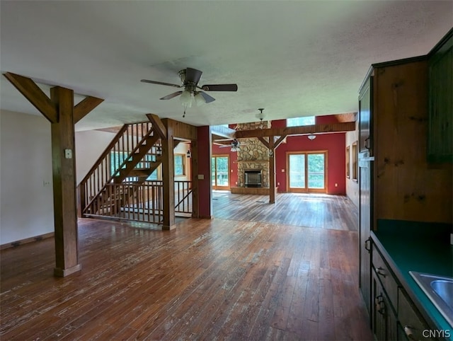 interior space featuring ceiling fan, sink, a textured ceiling, a stone fireplace, and dark wood-type flooring