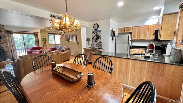 dining space with a fireplace, light wood-type flooring, sink, and an inviting chandelier