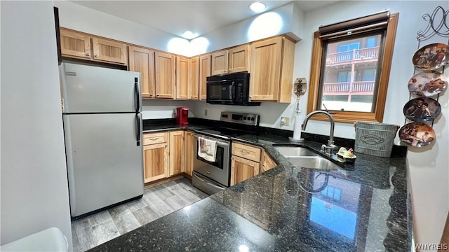 kitchen with appliances with stainless steel finishes, light hardwood / wood-style flooring, dark stone counters, and sink