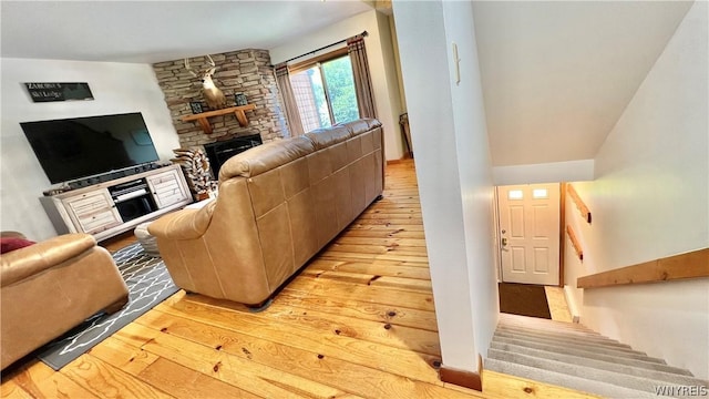 living room with light hardwood / wood-style floors, a stone fireplace, and lofted ceiling