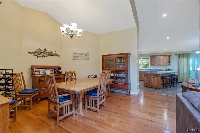 dining area with a chandelier, vaulted ceiling, and light hardwood / wood-style flooring