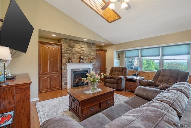 living room featuring light wood-style flooring, high vaulted ceiling, a skylight, ceiling fan, and a fireplace