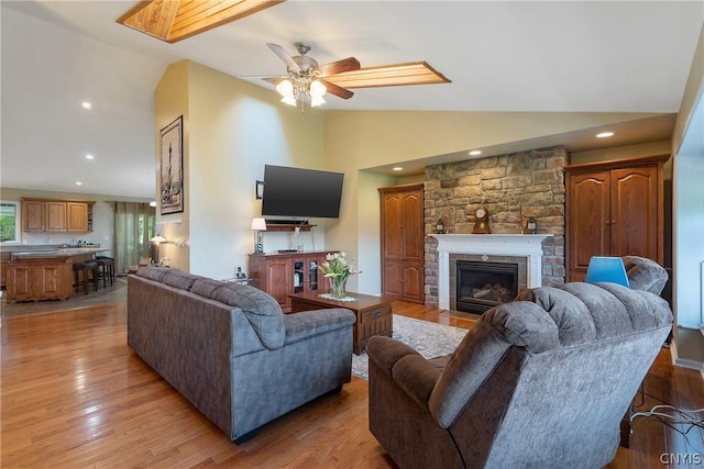 living room with a stone fireplace, ceiling fan, light hardwood / wood-style floors, and lofted ceiling