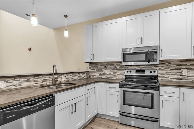 kitchen with tasteful backsplash, stainless steel appliances, sink, decorative light fixtures, and light wood-type flooring