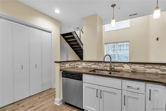 kitchen with stainless steel dishwasher, white cabinetry, hanging light fixtures, decorative backsplash, and light wood-type flooring