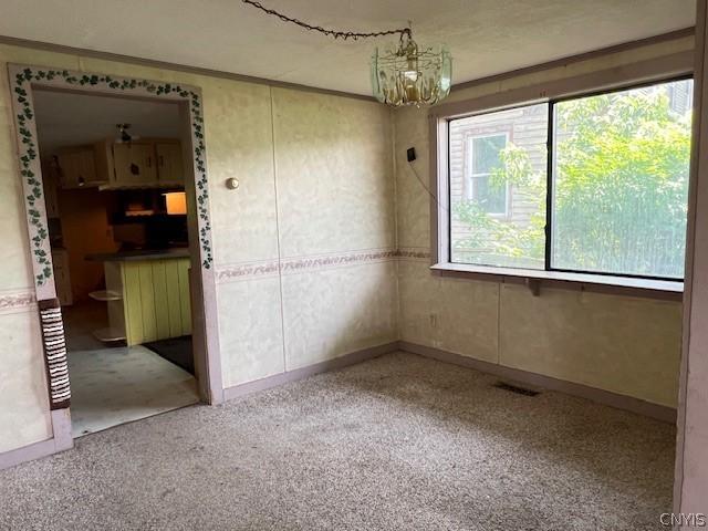 carpeted empty room featuring an inviting chandelier