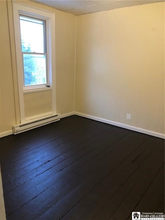 empty room featuring a baseboard radiator and dark hardwood / wood-style flooring