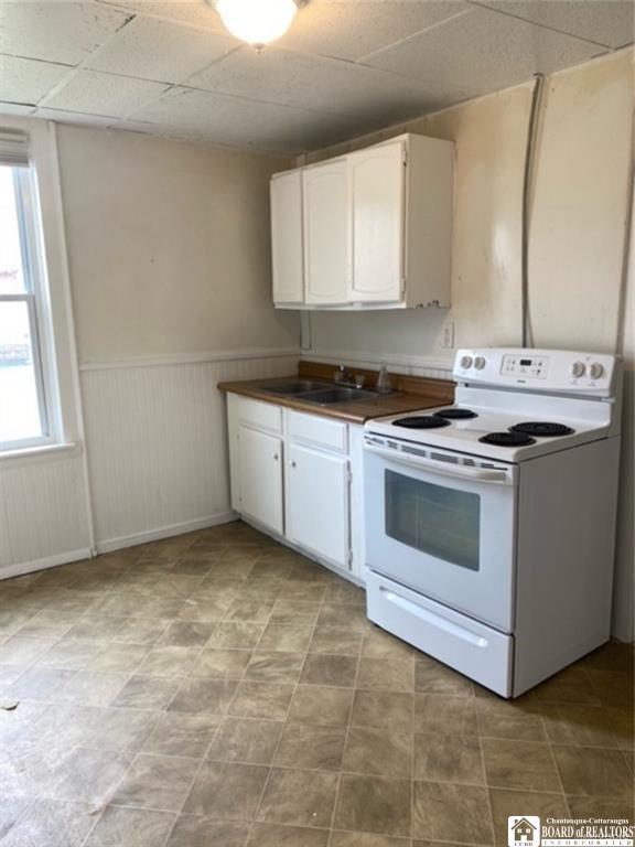 51 Fairmount Ave, Jamestown, NY 14701 - kitchen featuring white electric range, a sink, wainscoting, plenty of natural light, and white cabinets