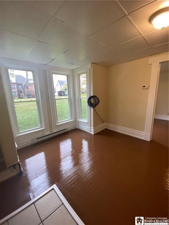 interior space featuring a drop ceiling, a baseboard heating unit, and dark hardwood / wood-style floors