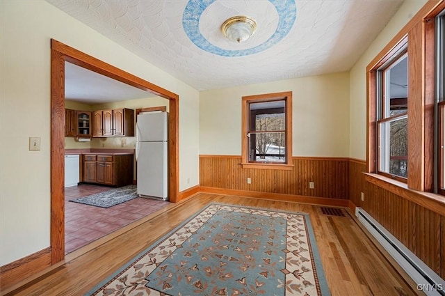 hall with a baseboard heating unit, wooden walls, a textured ceiling, and light hardwood / wood-style floors