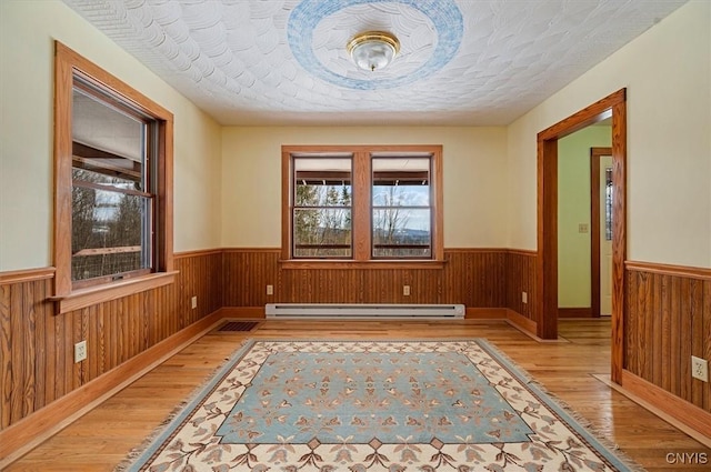 interior space featuring a baseboard radiator, light wood-type flooring, a textured ceiling, and wood walls