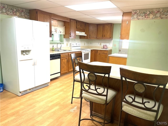 kitchen featuring backsplash, light hardwood / wood-style flooring, white appliances, and a paneled ceiling