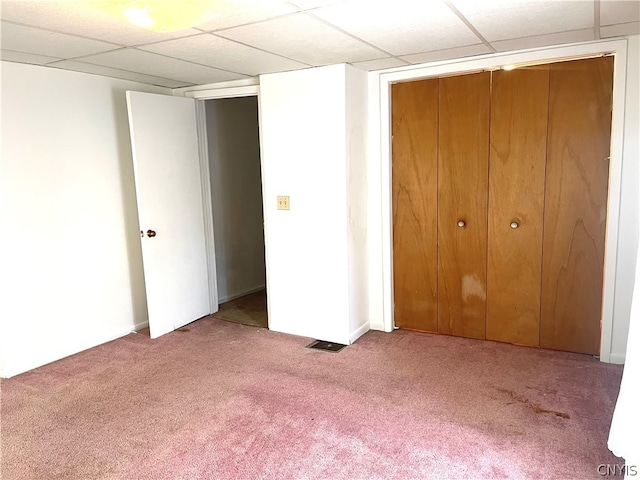 unfurnished bedroom featuring a drop ceiling, a closet, and carpet floors