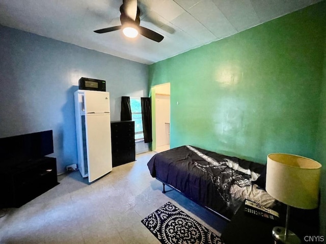 bedroom with concrete flooring, freestanding refrigerator, and a ceiling fan