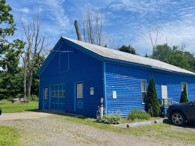 view of home's exterior with a yard, metal roof, driveway, and a detached garage