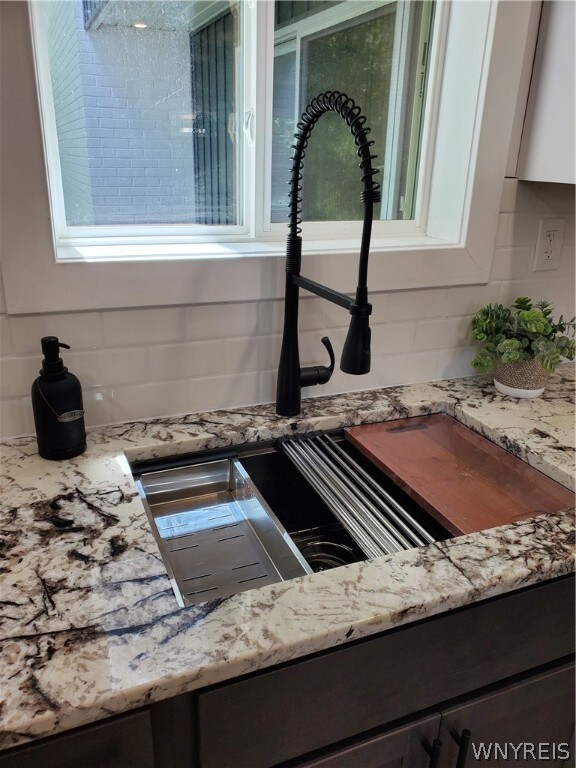 details with white cabinetry, dark brown cabinets, sink, light stone countertops, and backsplash