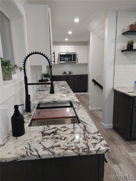 kitchen featuring white cabinetry, tasteful backsplash, light wood-type flooring, light stone counters, and sink