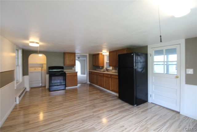 kitchen featuring washing machine and dryer, light hardwood / wood-style flooring, baseboard heating, and black appliances