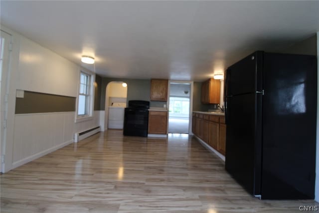 kitchen with a healthy amount of sunlight, black appliances, a baseboard radiator, and light wood-type flooring